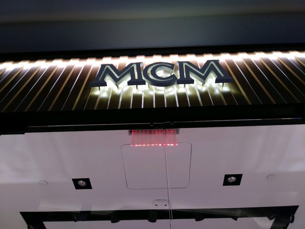 MCM Halo Lit Sign Black dimensional letters on striped black and gold backing