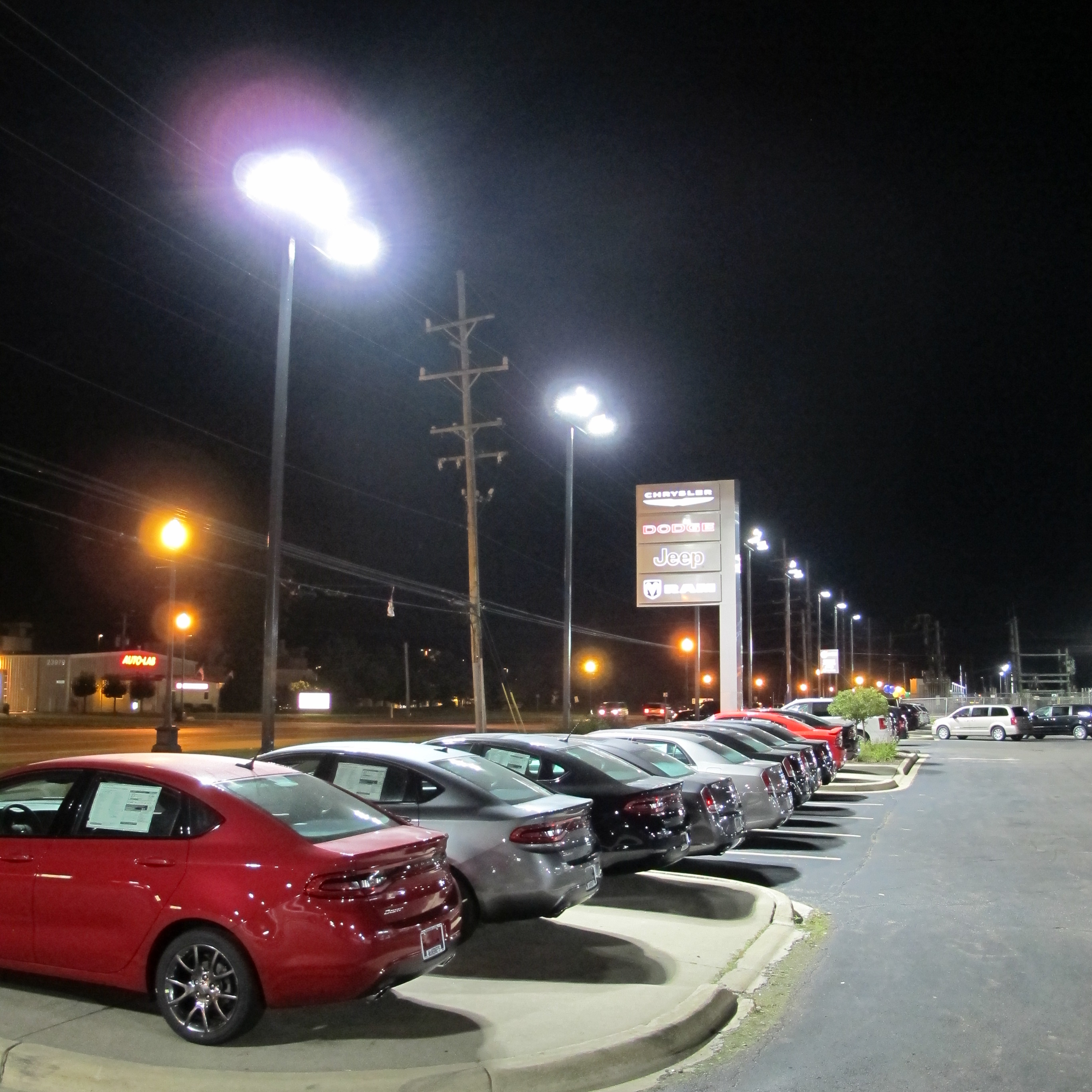 McInerneys Car Dealership Lot Lighting pictured with row of cars and pylon road sign